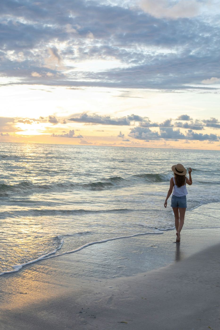 A woman in a sun hat walking along the shore at dusk