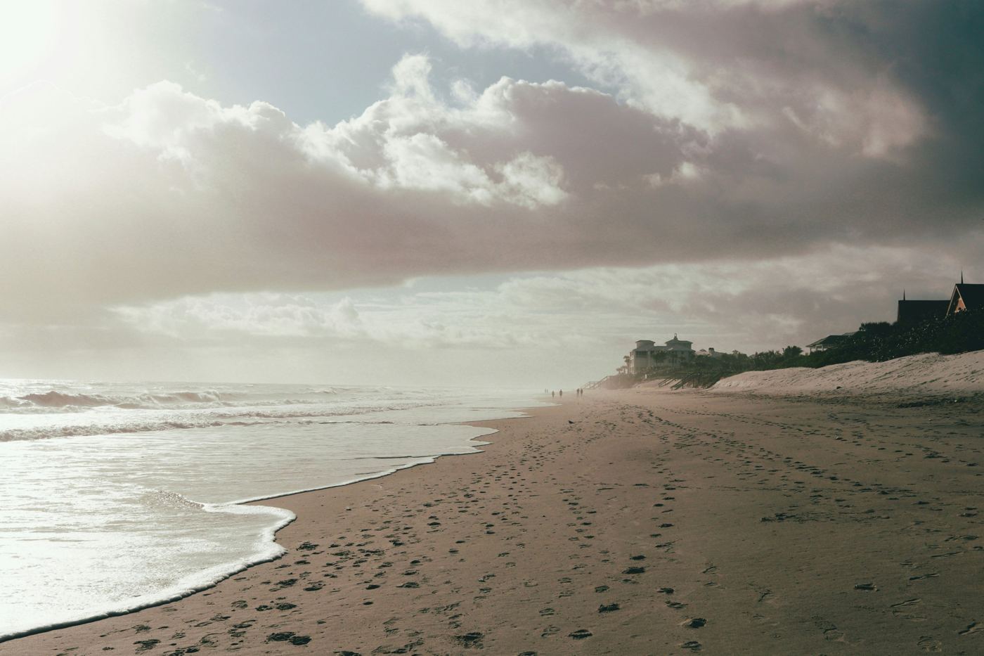 A pale beach under soft cloud, walkers small along the shore