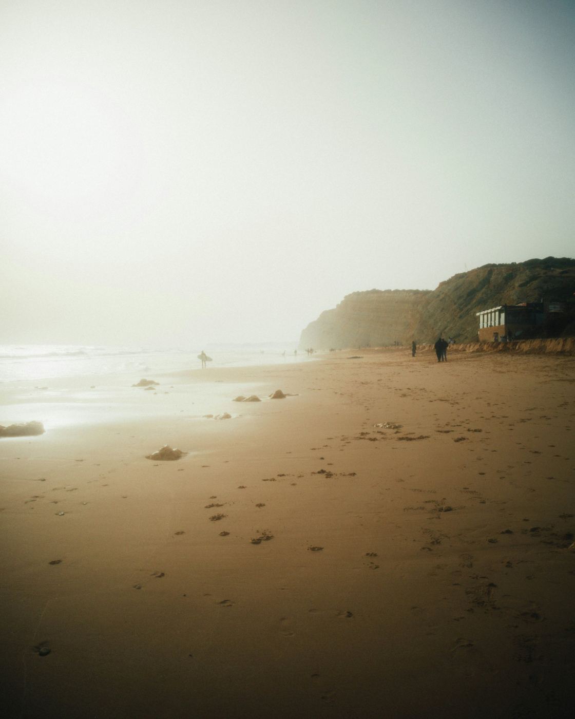 A hazy beach beneath sandstone cliffs, walkers small in the distance
