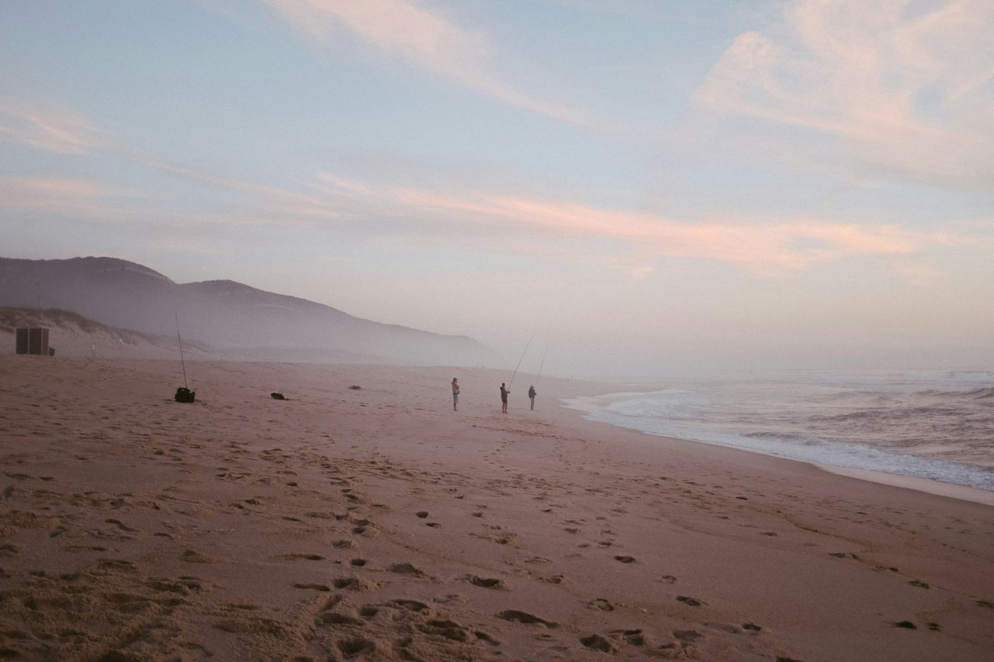 Three people fishing together on a misty beach at dawn